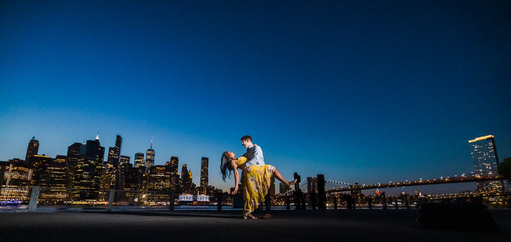 woman in yellow dress being dipped by man with Brooklyn Bridge and FiDi in background