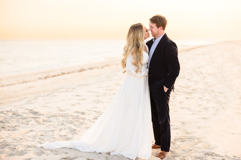 woman in white dress on beach rubbing noses with man in suit at sunset