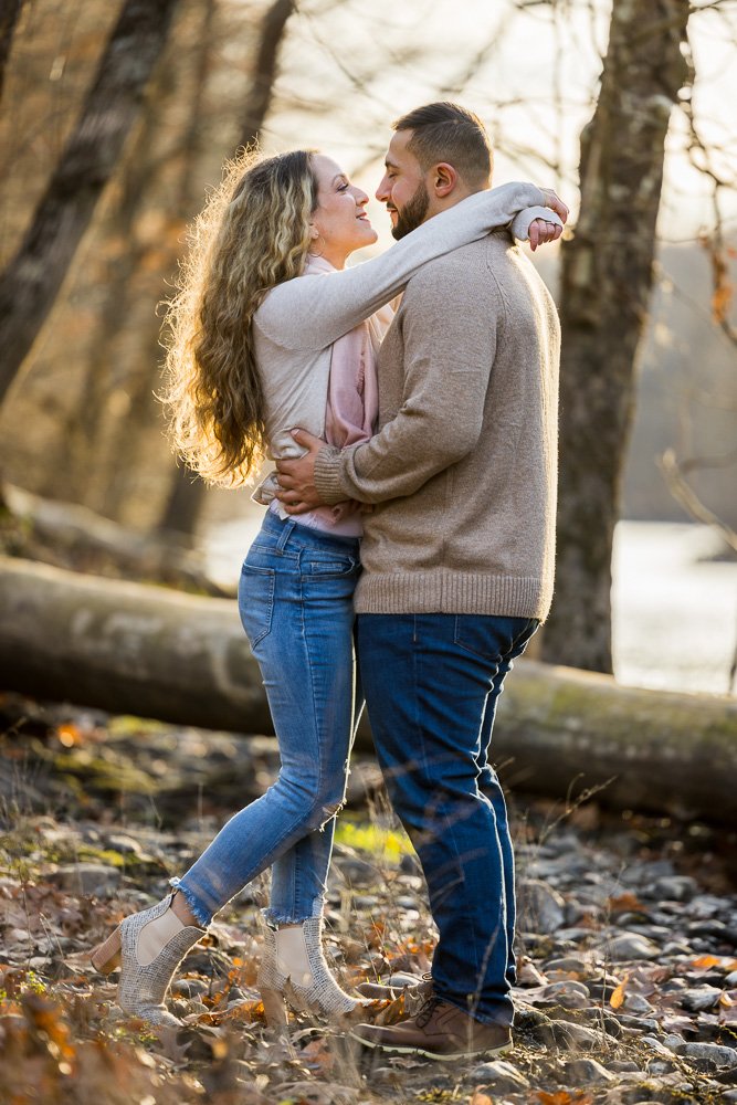 couple in woods holding each other next to river in fall