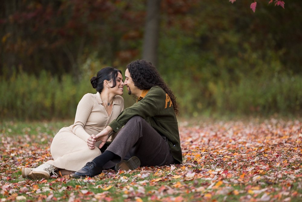 couple sitting on leaves with beige dress and green shirt rubbing noses