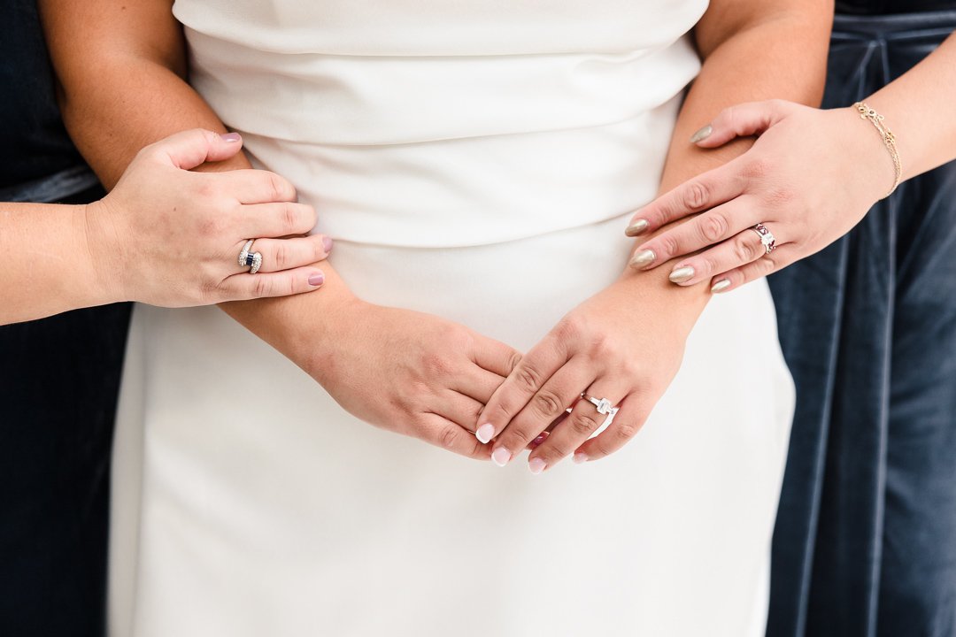 close up of brides hands with sisters hands holding forearm