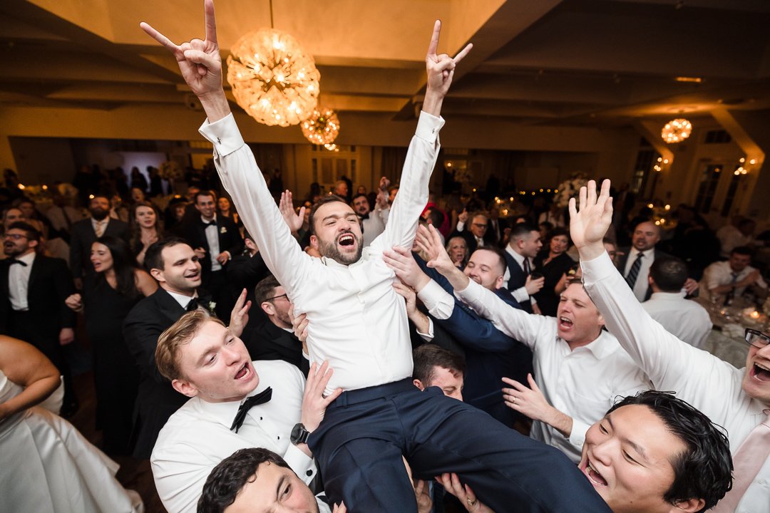 groom being lifted by friends at reception at heritage club