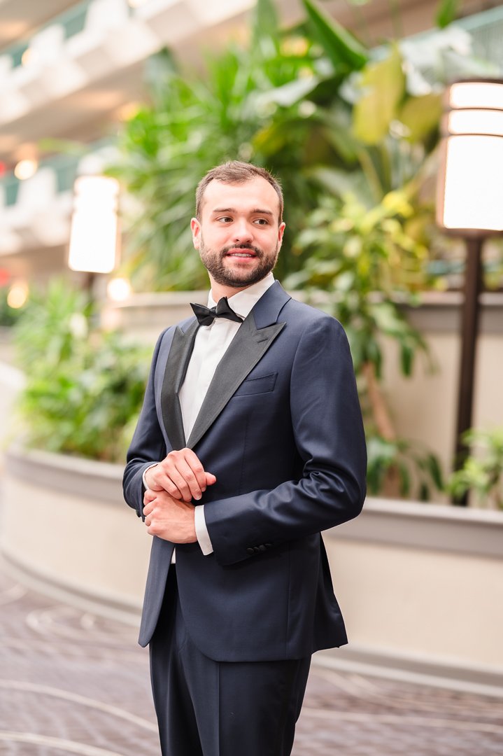 groom looking past camera in hotel lobby with foliage