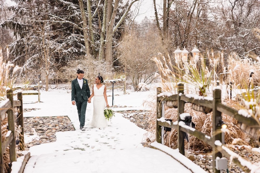 bride and groom walking over bridge in snow