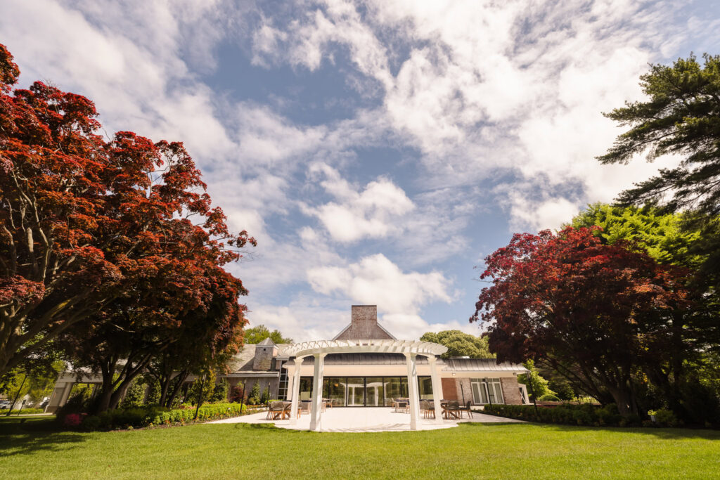 Exterior view of an elegant Long Island wedding venue framed by mature trees, manicured lawn, and a white pergola.