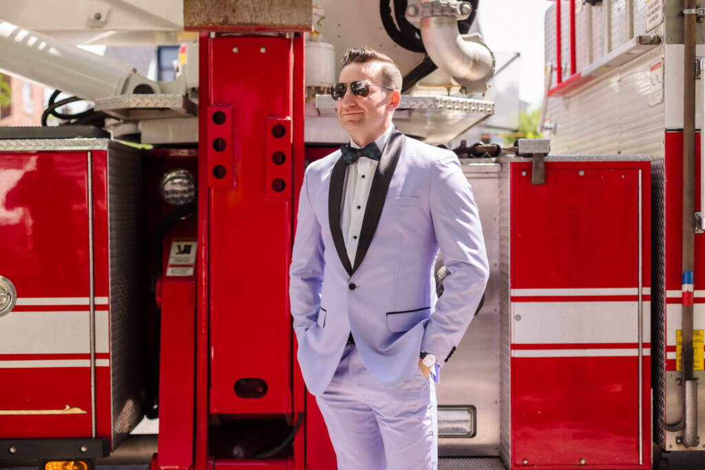 Groom with sunglasses in front of fire truck.