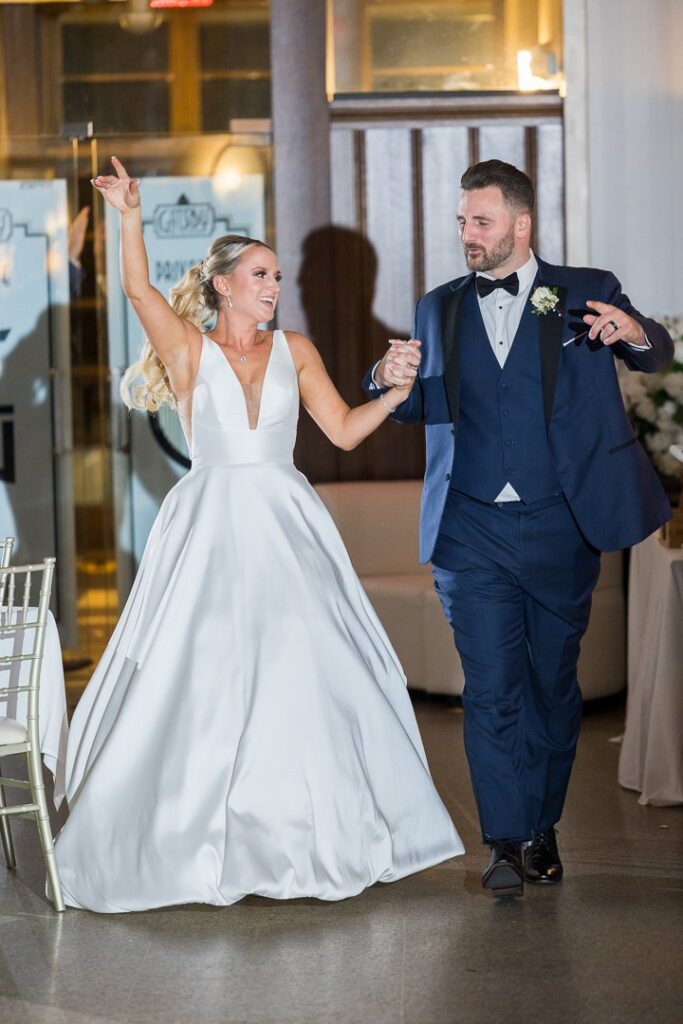 Bride and groom entering reception while raising their hands in the air