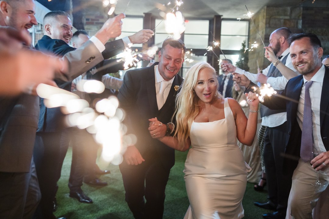 Bride and groom walking out of Gatsby on the Ocean between rows of sparklers.