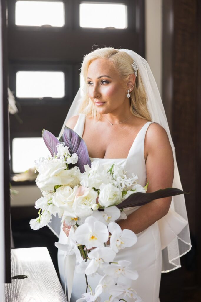 bride holding bouquet and looking out the window in bridal suite at Gatsby on the Ocean