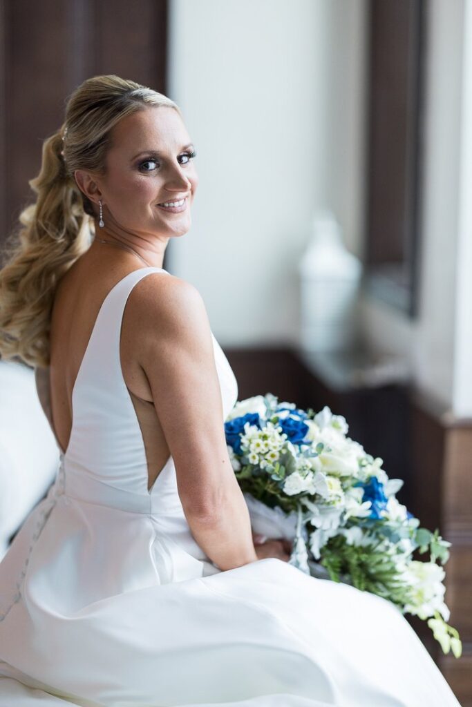 Bride in wedding dress sitting in bridal suite with flowers at Gatsby on the Ocean