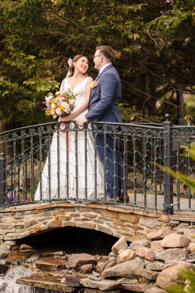 Bride and groom looking at each other on stone bridge at Fox Hollow.
