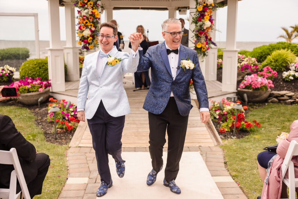 Two grooms walking down the aisle celebrating after the ceremony.