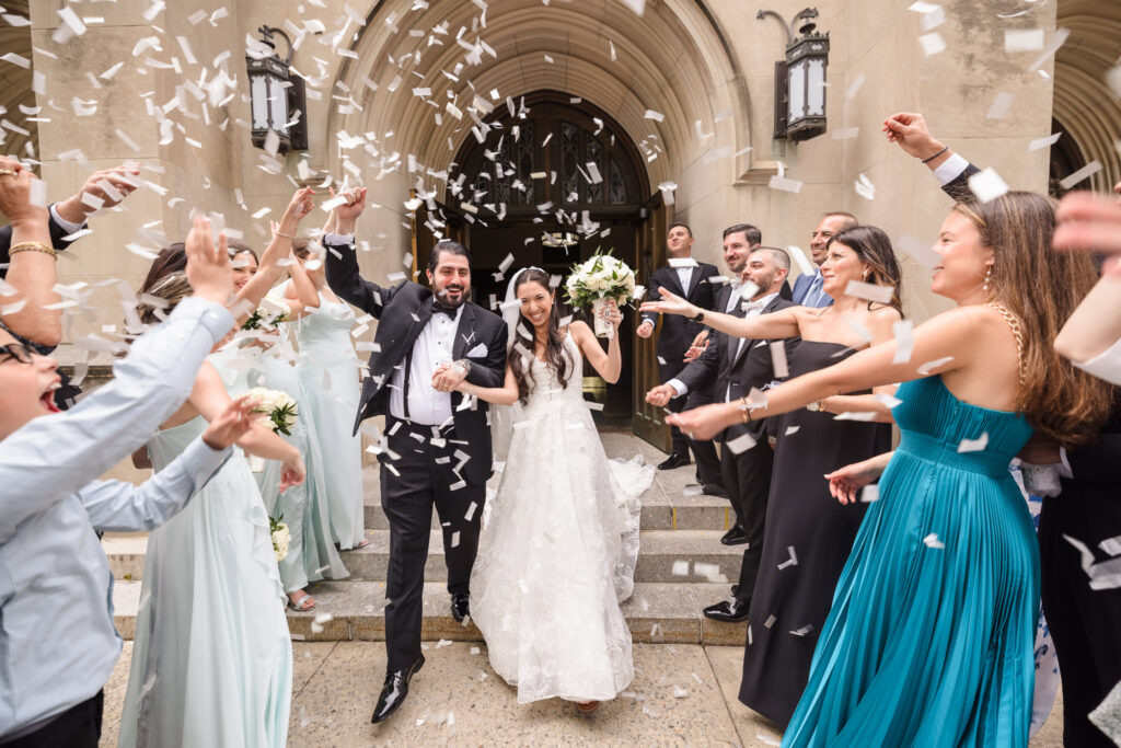 bride and groom walking out of church while bridal party throws confetti