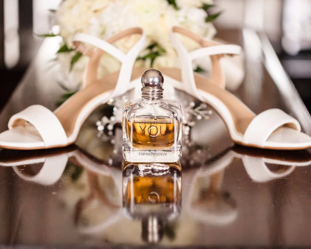 shoes, perfume, and bouquet on a shiny surface during wedding preparation