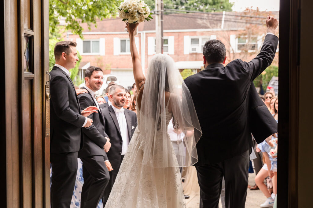 bride and groom from behind as they leave the church with their hands in the air