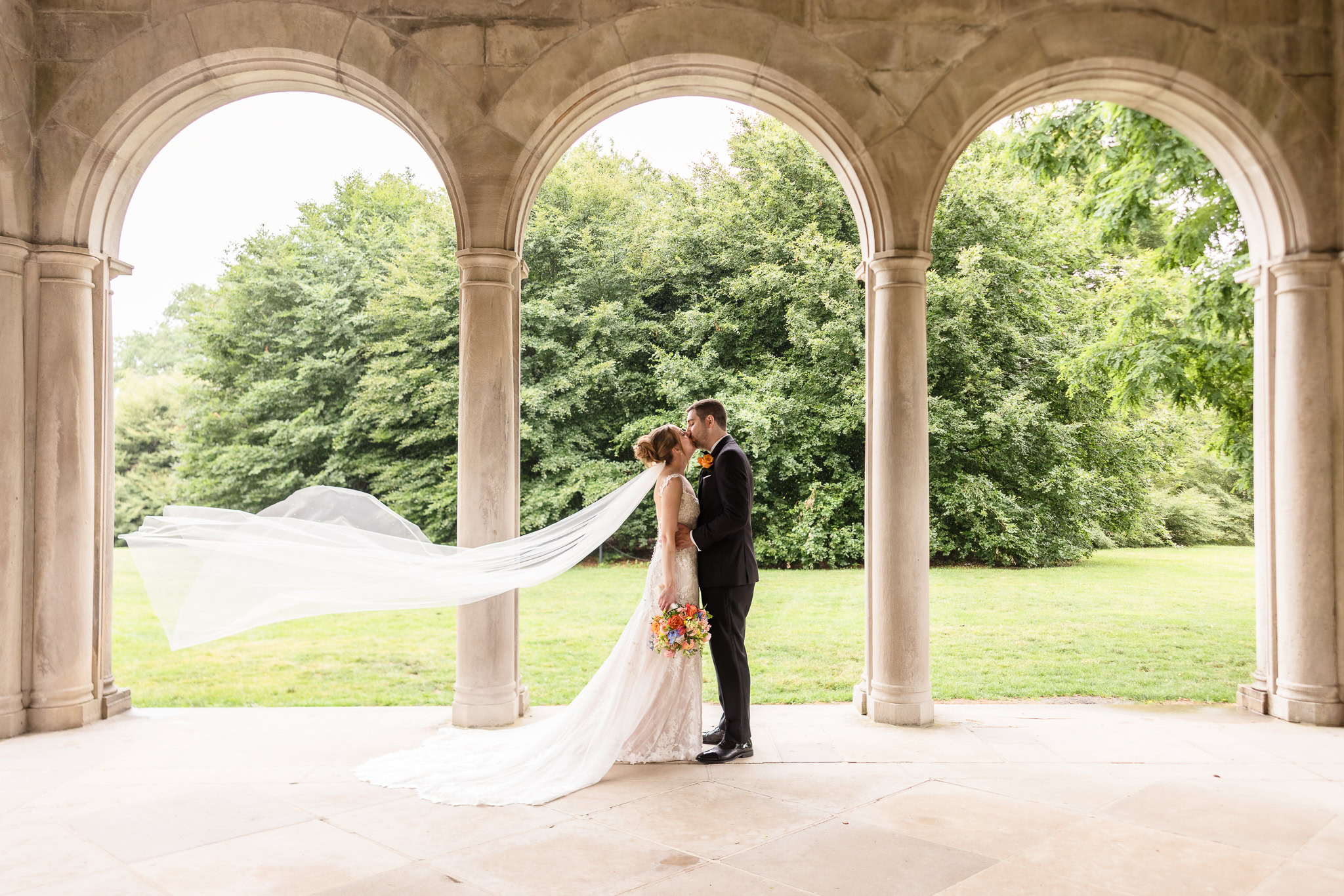 Bride and groom sharing a quiet moment beneath the stone arches at Planting Fields Arboretum on Long Island.