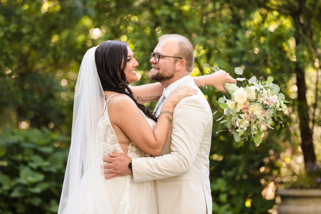 Bride and groom embracing in Majestic Gardens with bride holding bouquet over groom's shoulder.