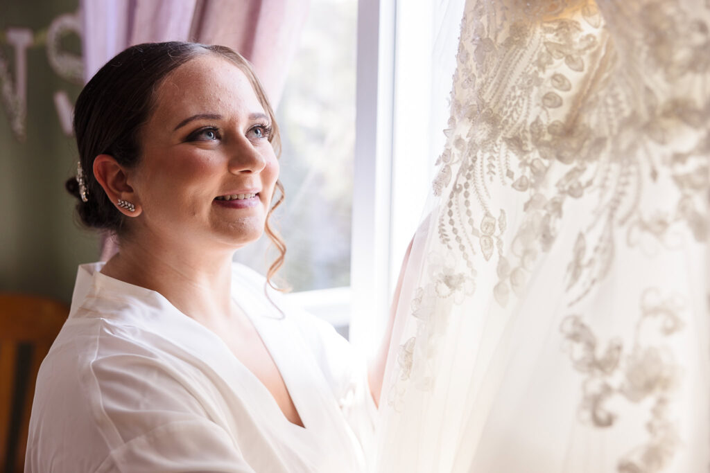 Bride looking at her wedding dress hanging in the window.