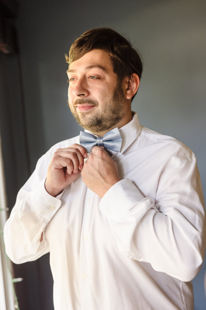 Groom fixing his bow tie.