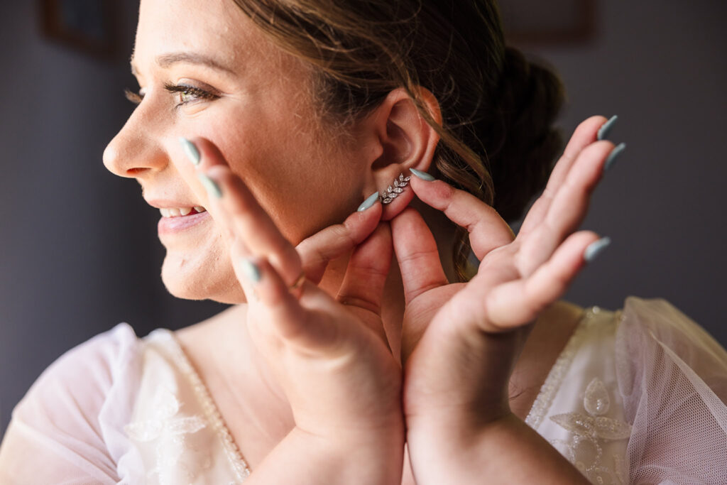 Close up of bride smiling while putting on earrings.