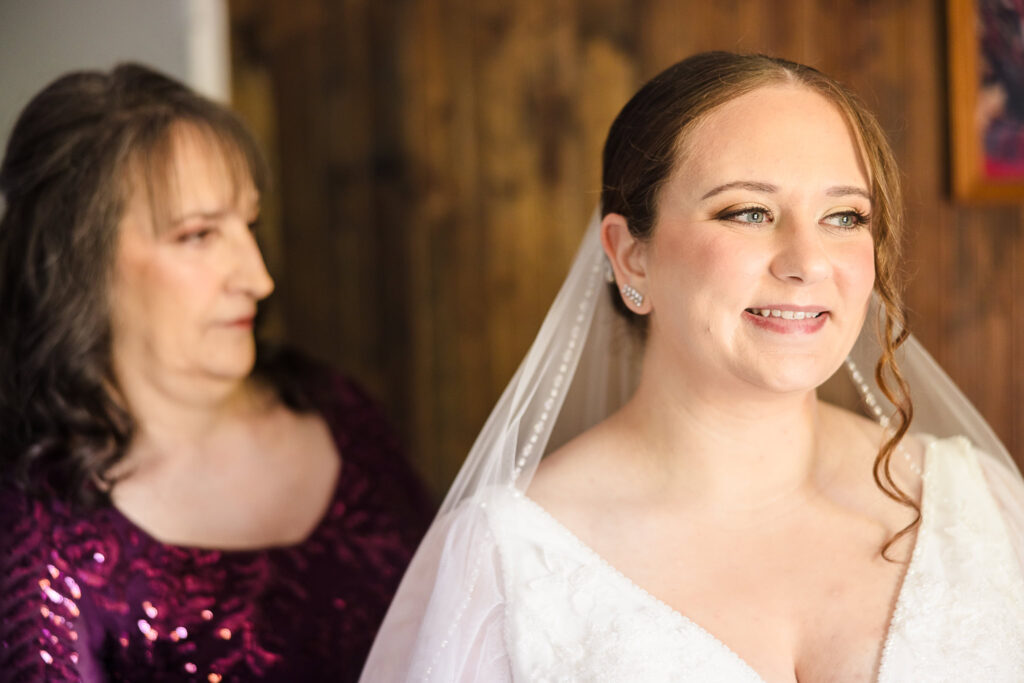 Bride smiling while mom helps her button wedding dress.