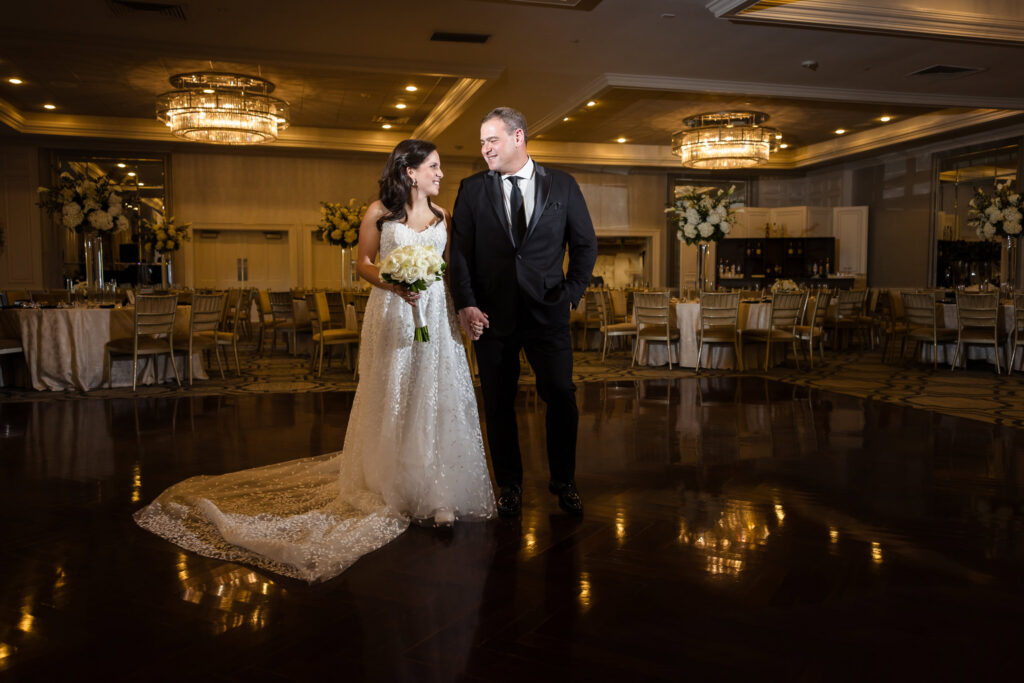 Bride and groom holding hands on the dance floor inside the reception room at Glen Head Country Club.