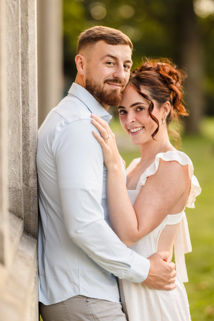 Woman and man embracing while looking at the camera at Planting Fields Arboretum.