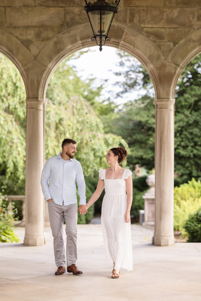 Woman and man holding hands under arch at Planting Fields Arboretum mansion.