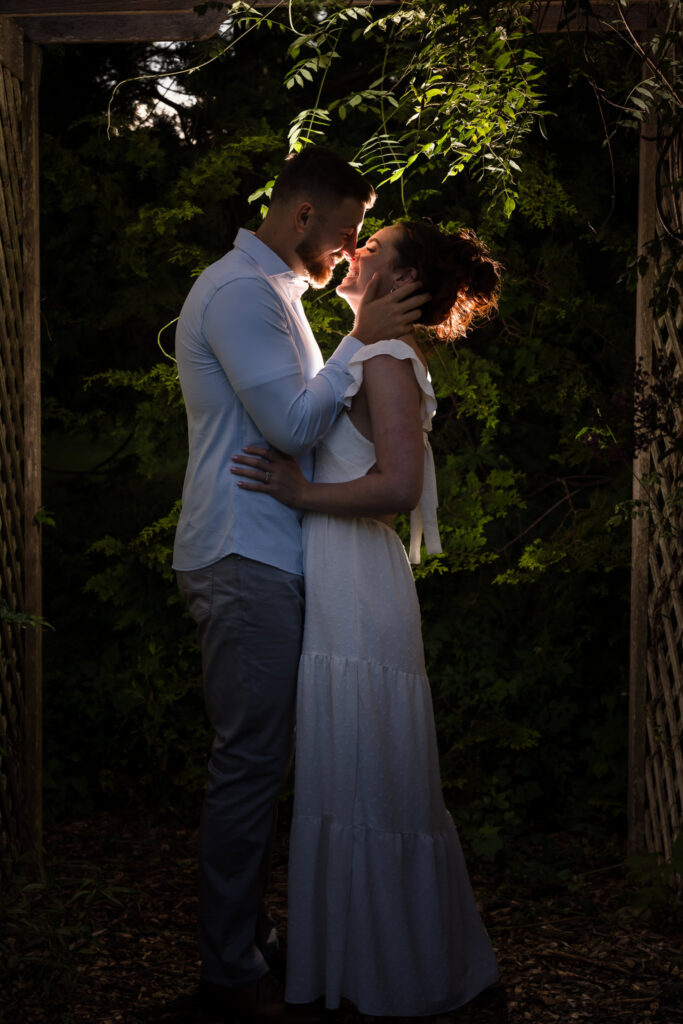 Man and woman kissing under arch while being backlit.