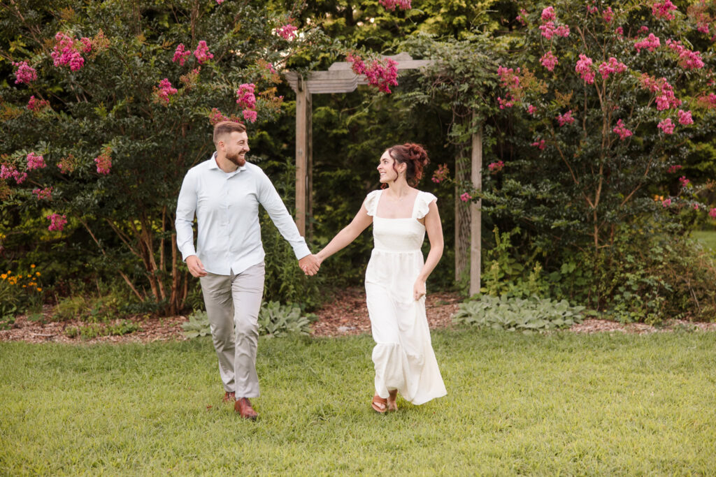 Woman and man looking at each other, holding hands, and smiling at their engagement session at Planting Fields Arboretum.