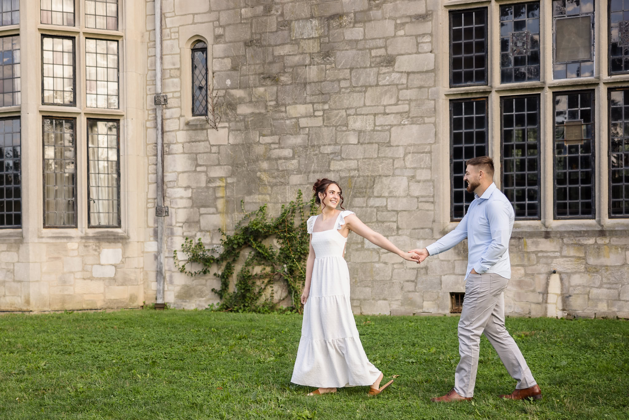 Woman in long dress leading a man in blue shirt in front of the mansion at Planting Fields Arboretum.