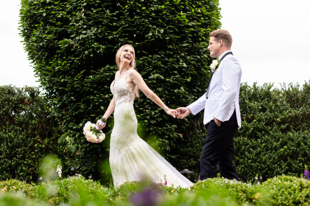 Bride and groom holding hands and laughing together in the landscaped gardens at Larkfield.