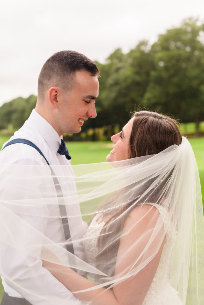 Bride and groom smiling at each other with bride's veil covering their bodies. 