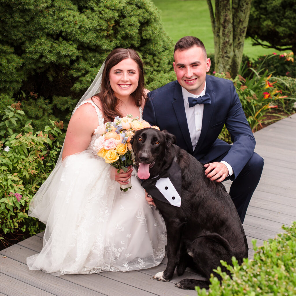 Bride and groom squatting with dog at Rock Hill Country Club. Everyone is smiling at the camera.