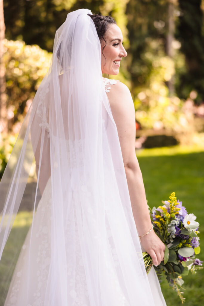 Bride from behind looking to the right and holding a bouquet at Fox Hollow.