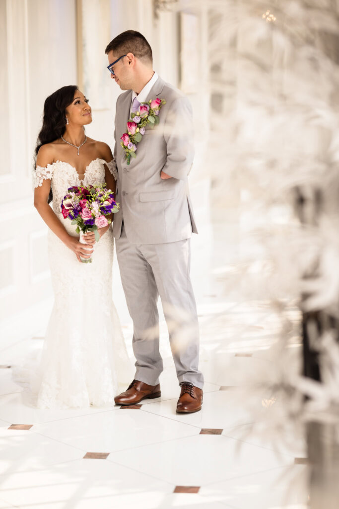 Bride and groom smiling at each other in a white hallway at The Choral House.