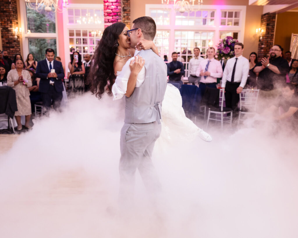 Bride and groom during first dance at The Coral House. The groom is lifting and spinning the bride, and the floor is filled with smoke. 