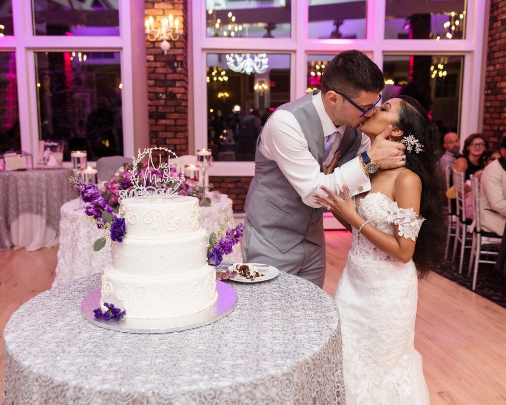 Bride and groom kissing next to their wedding cake. 