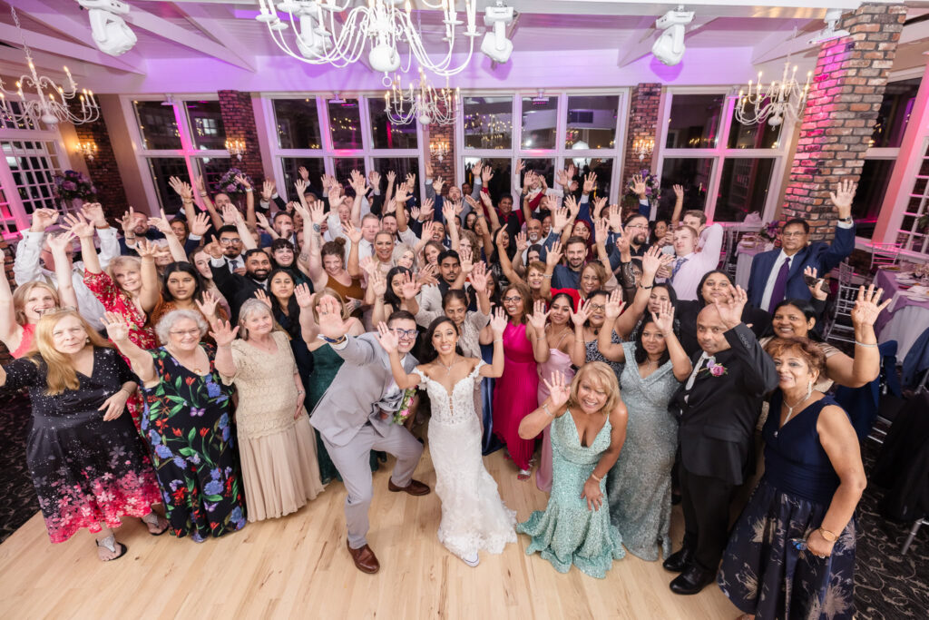 Bride and groom with everyone at the wedding on the dance floor smiling at the camera.