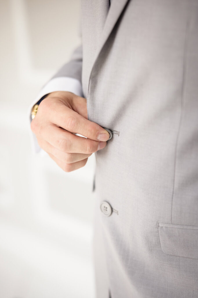 Close up image of groom buttoning jacket at The Choral House.