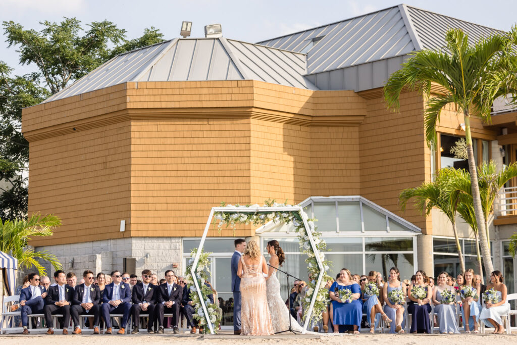 Wide shot of wedding ceremony with The Crescent Beach club behind the guests. 