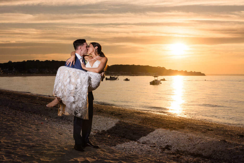 Groom holding bride and kissing on the shore during sunset at The Crescent Beach Club.