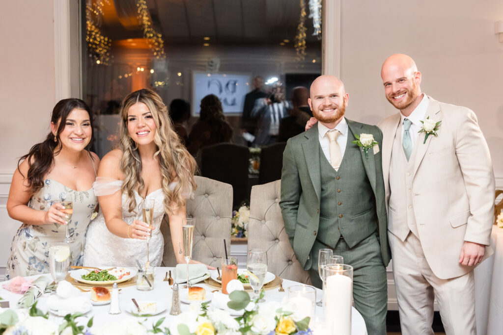 Maid of honor, best man, bride, and groom smiling at the camera after speeches. 