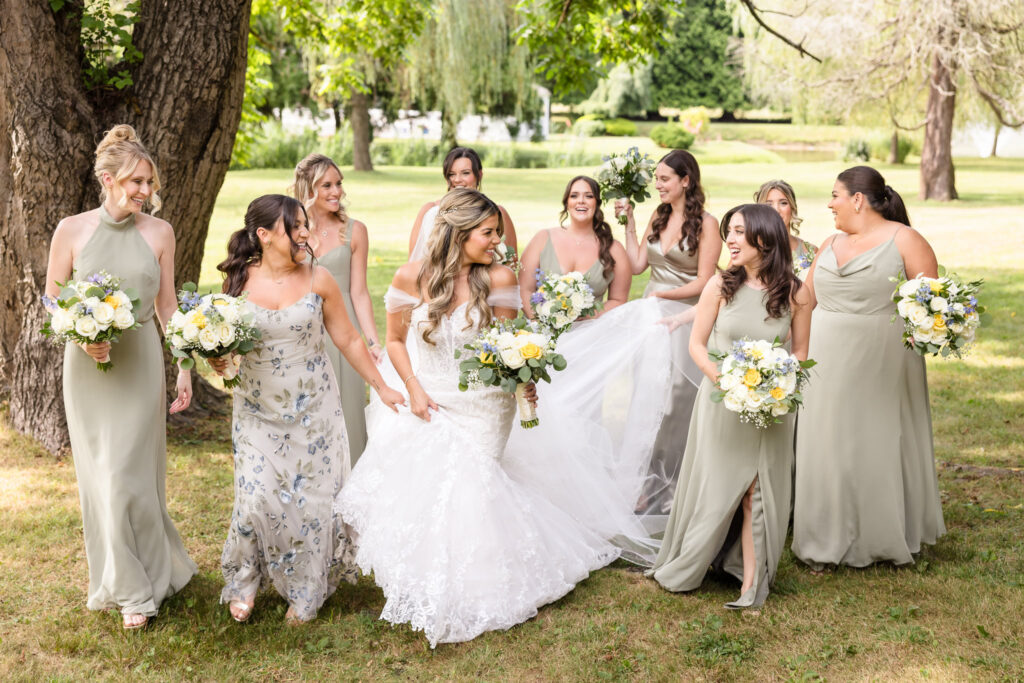 Bride at Flowerfield walking with bridesmaids holding her train, walking, and laughing. 