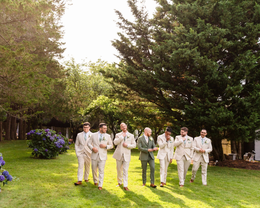 Groom and groomsmen on grounds of Flowerfield walking and adjusting their ties.