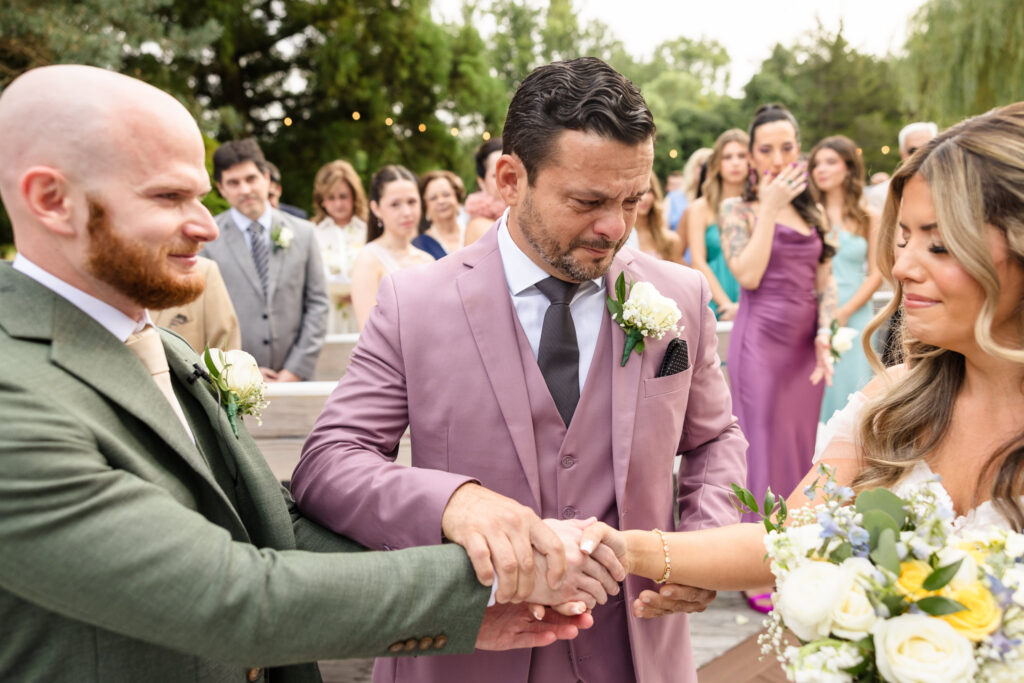 Bride holding hands with bride and groom at outdoor wedding ceremony at Flowerfield. 