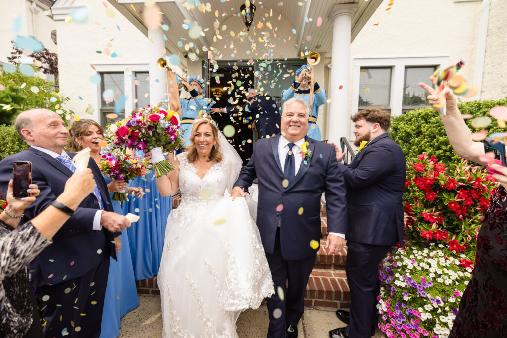 Bride and groom exiting the church while confetti is being thrown. The couple and everyone else is laughing.