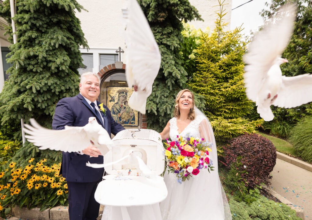 Bride and groom smiling while doves are getting released.