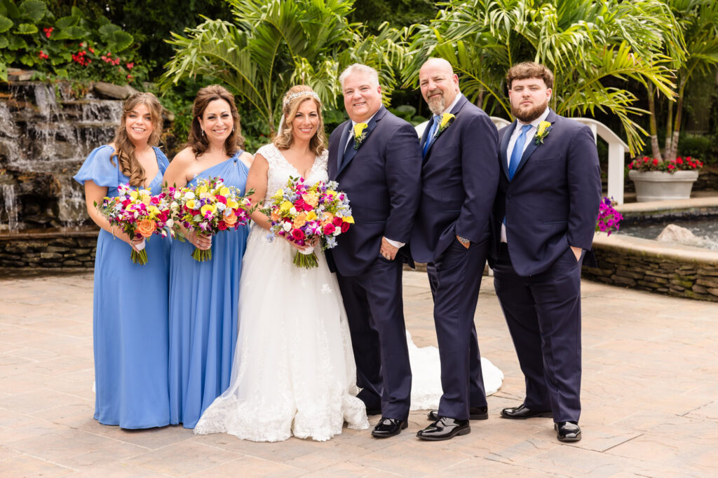 Bridal party with bride and groom smiling at the camera in the garden of Sand Castle.