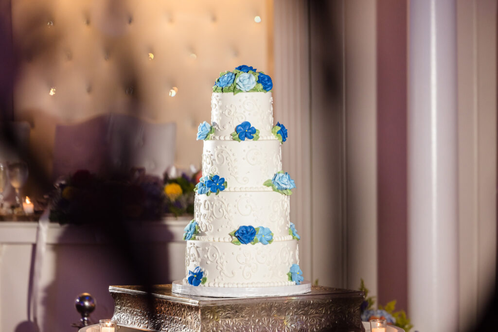 Four tier wedding cake with dark and light blue flowers at Sand Castle.